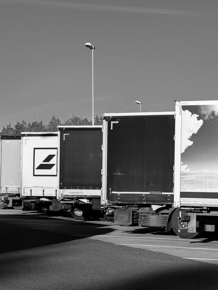 Home Black and white photo of semi trucks parked in a row at a loading area outdoors.